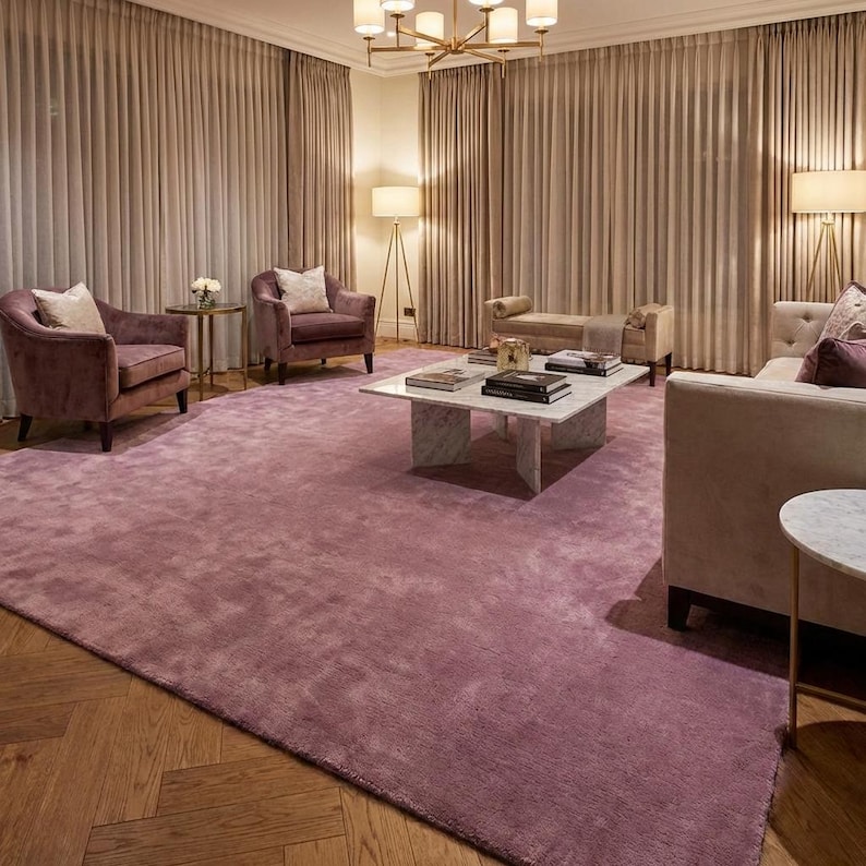 Puede incluir: Un lujoso sal&oacute;n con una gran alfombra suave de color malva. La habitaci&oacute;n incluye dos sillones, un sof&aacute; y una mesa de centro. Las paredes est&aacute;n adornadas con cortinas de tonos neutros, y la habitaci&oacute;n est&aacute; iluminada por una l&aacute;mpara de ara&ntilde;a y l&aacute;mparas de pie.