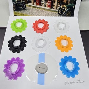 May include: A collection of eight flower-shaped adhesive covers in lime green, red, white, black, translucent, orange, purple, and blue, plus one gray Dexcom G7 sensor with a clear adhesive patch. The text Dexcom G7 only is written in the corner.