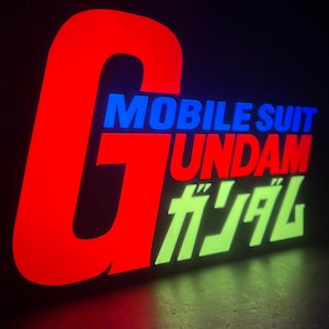 以下が含まれることがあります： 赤、青、緑で「ガンダム」の文字が入った電飾看板。左側には大きな赤い「G」があり、その上に青で「MOBILE SUIT」、赤で「UNDAM」と書かれています。緑色の日本語の文字。