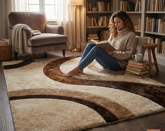 Può includere: Un tappeto beige e marrone con un motivo a spirale. Il tappeto presenta una texture morbida e soffice e un design di fasce curve in varie tonalità di marrone. Il tappeto è posizionato su un pavimento in legno scuro.