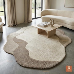 Nowoczesny ręcznie tkany dywan wełniany, organiczny kształt, neutralny kremowo-beżowy, abstrakcyjny wzór kałuży