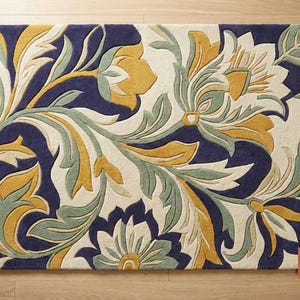 May include: Rectangular rug with a floral design. The rug features a navy blue background with cream, yellow, and sage green floral patterns. The design includes stylized flowers and leaves, creating a decorative and artistic look. The rug is placed on a wooden floor.