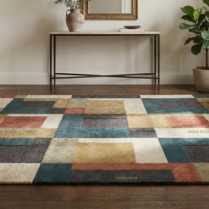 May include: A rectangular area rug with a geometric pattern in shades of teal, rust, beige, and gray. The rug features a patchwork design with various rectangular and square shapes. The words "UNIQUE RUGS" are visible on the rug.
