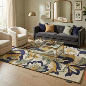 May include: A living room scene featuring a gray sofa, two cream-colored armchairs, and a patterned rug with blue, yellow, and green floral designs. A gold-framed coffee table and mirror add elegance. A floor lamp and potted plant complete the decor.