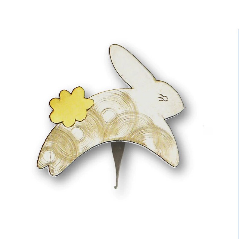 May include: A white bunny-shaped bottle stopper with a yellow flower accent. The bunny has gold swirl details and a silver stem. A decorative item for wine bottles.