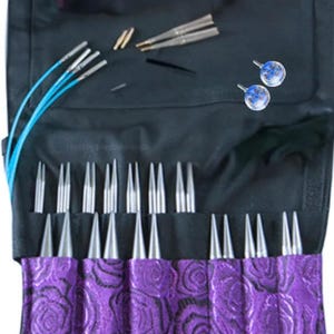 May include: A black knitting needle case with a purple rose pattern. The case is open, showing various knitting needles, cables, and accessories. The needles are silver and the cables are blue. Two blue and white stitch markers are also visible.