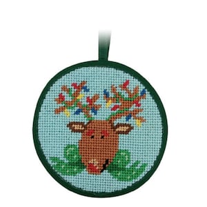 May include: A round Christmas ornament featuring a cross-stitched reindeer design. The reindeer has brown antlers adorned with colorful lights, a brown face, and a green bow. The ornament has a green border and a green ribbon for hanging.