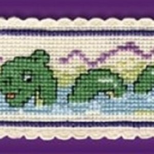 May include: A cross-stitch bookmark kit featuring a green Loch Ness Monster, or Nessie, in a lake with purple mountains in the background. The kit includes a white fabric with a scalloped edge and a needle. The text "Nessie" is stitched in red thread.