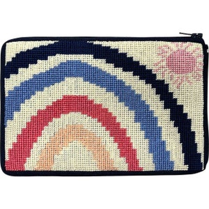 Op de afbeelding: Een rechthoekig, met de hand gestikt etui met een marineblauwe ritssluiting en rand. Het ontwerp toont een regenboogboog in tinten rood, blauw en cr&egrave;me, met een roze zon in de rechterbovenhoek. Het etui is waarschijnlijk gemaakt van canvas of een vergelijkbaar materiaal.