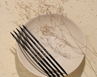 May include: Five black knitting needles with gold lettering on a white plate. The lettering reads "LANTERN MOON" and "US8/5.0mm".