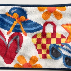 Op de afbeelding: Een rechthoekig, wit naaldkunst etui met een marineblauwe rits en rand. Het ontwerp toont een blauwe zonnehoed, rode slippers, een geruite picknickmand, zonnebrillen, een zeester en oranje bloemen, allemaal in een strandthema.