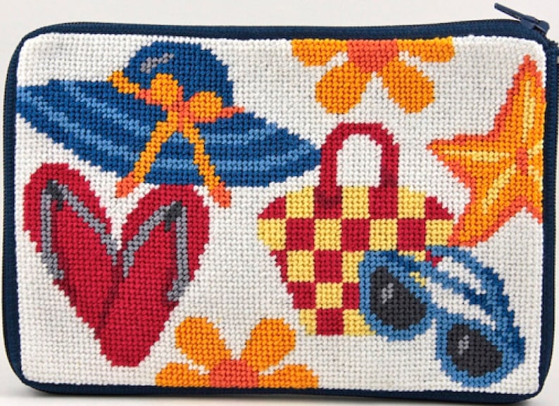 Op de afbeelding: Een rechthoekig, wit naaldkunst etui met een marineblauwe rits en rand. Het ontwerp toont een blauwe zonnehoed, rode slippers, een geruite picknickmand, zonnebrillen, een zeester en oranje bloemen, allemaal in een strandthema.