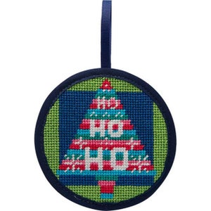 May include: A round Christmas tree ornament with a stitched design. The tree is blue, red, and white, with the word "HO" stitched on it. The ornament has a green background and a blue border with a blue ribbon for hanging.