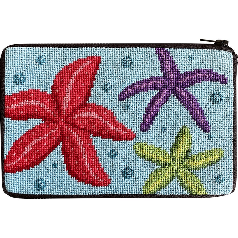 Op de afbeelding: Een rechthoekig etui met ritssluiting met een lichtblauwe achtergrond en een borduurontwerp met drie zeesterren. De zeesterren zijn rood, paars en groen. Het etui heeft een zwarte rand en ritssluiting.