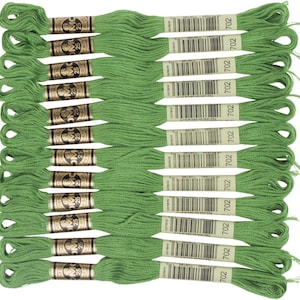 May include: A collection of green embroidery floss skeins, arranged in neat rows. Each skein is labeled with the number 702 and the brand name DMC. The floss is a vibrant, medium green color, perfect for various needlework projects.