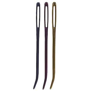May include: Three plastic yarn needles in different colors: purple, gold, and blue. The needles are long and thin with a small eye at the top.