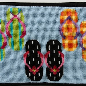 Op de afbeelding: Een lichtblauwe, kruissteek etui met ritssluiting met een kleurrijk ontwerp van slippers. De slippers zijn in verschillende kleuren, waaronder groen, oranje en zwart, met roze en paarse bandjes. De etui heeft een zwarte ritssluiting en afwerking.