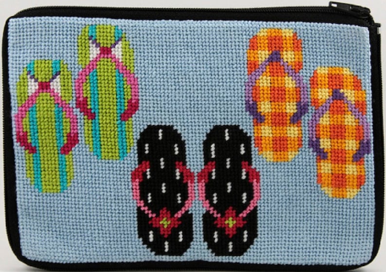 Op de afbeelding: Een lichtblauwe, kruissteek etui met ritssluiting met een kleurrijk ontwerp van slippers. De slippers zijn in verschillende kleuren, waaronder groen, oranje en zwart, met roze en paarse bandjes. De etui heeft een zwarte ritssluiting en afwerking.