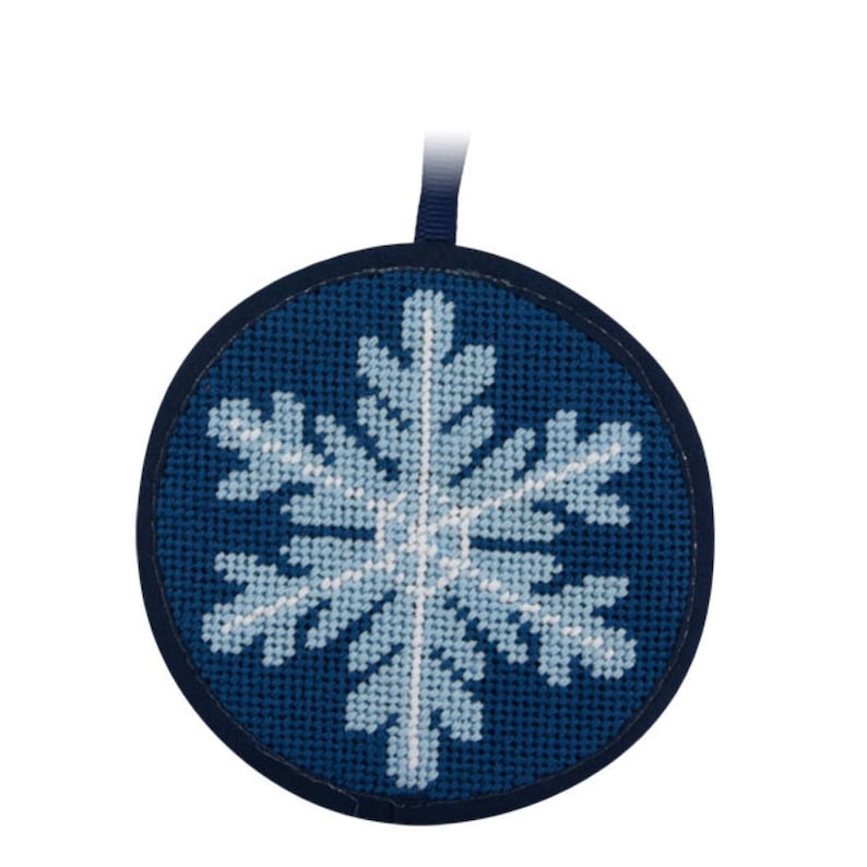 May include: A round, navy blue Christmas ornament with a light blue and white snowflake design. The snowflake is created with cross-stitch embroidery. A dark blue ribbon is attached for hanging.