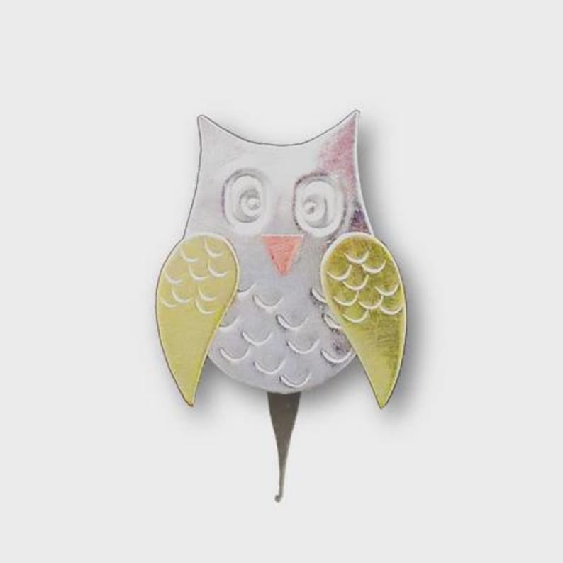 May include: A silver-colored owl-shaped garden stake with yellow wings and a pink beak. The owl has large, round eyes and a textured body. The stake is designed to be inserted into the ground.