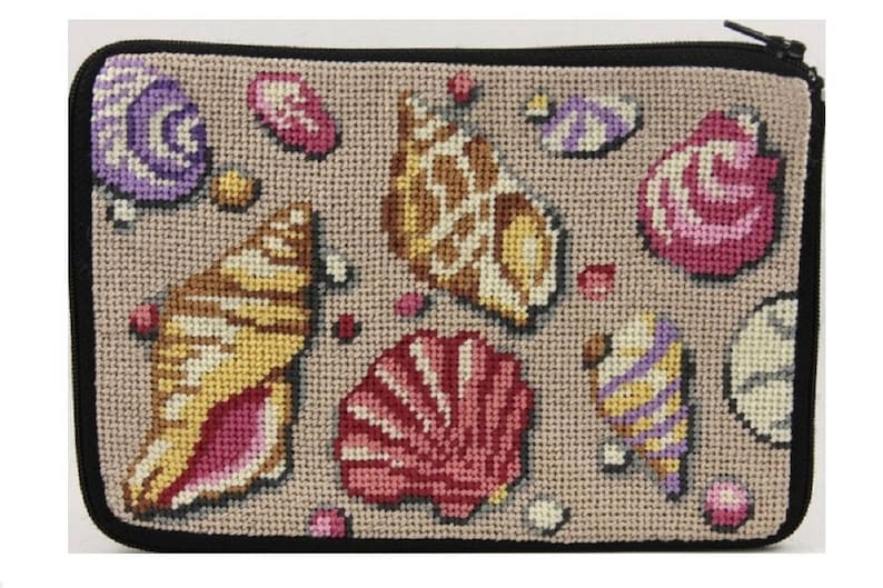 Op de afbeelding: Een beige etui met ritssluiting en zwarte rand, met een kruissteekontwerp van verschillende schelpen in tinten geel, roze, paars en bruin. De schelpen zijn verspreid over het oppervlak.