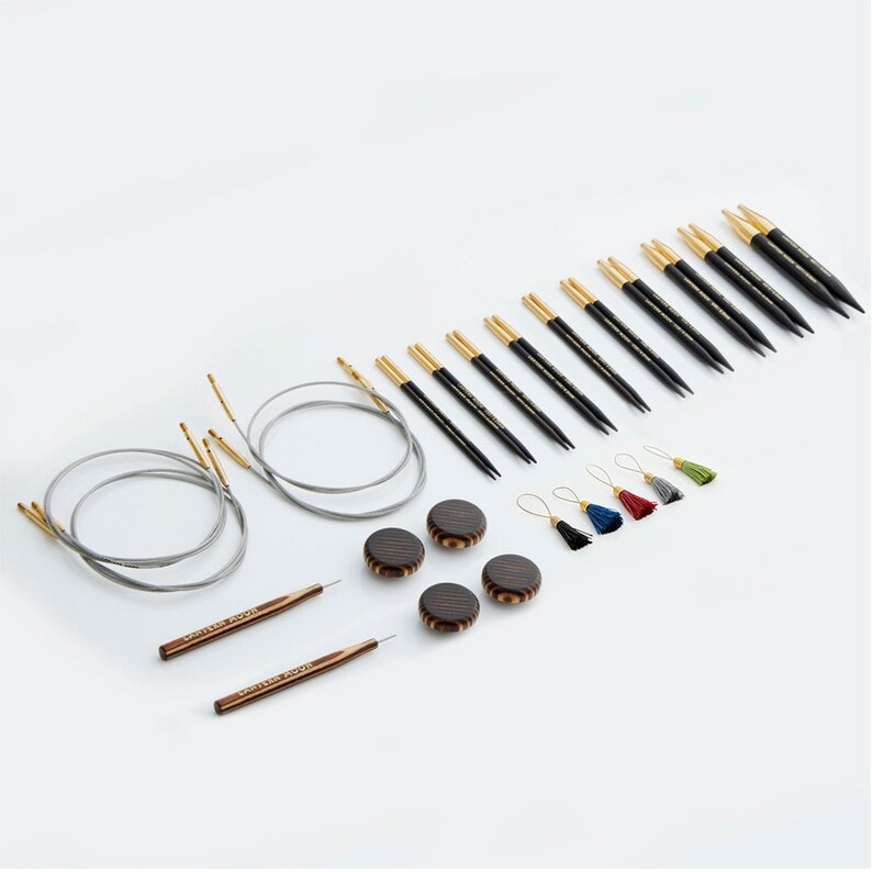 May include: A set of interchangeable circular knitting needles with black and gold tips, wooden cable ends, and a set of four wooden stitch markers. The needles are arranged in order of size, with the smallest needles at the top and the largest needles at the bottom. The stitch markers are in a variety of colors, including red, blue, green, and gray.