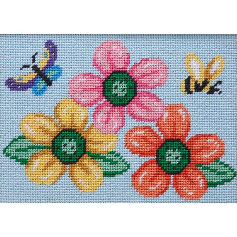 Pode incluir: Um desenho de ponto de agulha com tr&ecirc;s flores coloridas com folhas verdes e uma abelha amarela e preta sobre um fundo azul claro.