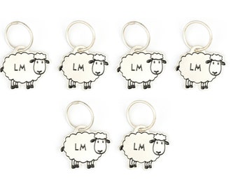 May include: Five white sheep keychain charms with black eyes, noses, and legs. Each charm has a silver key ring and the initials "LM" printed on the sheep's body.