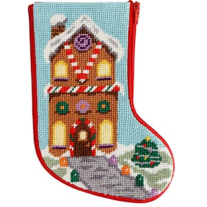May include: A needlepoint Christmas stocking features a gingerbread house with candy cane trim, a wreath, and a small Christmas tree. The stocking is red and white with a blue background.