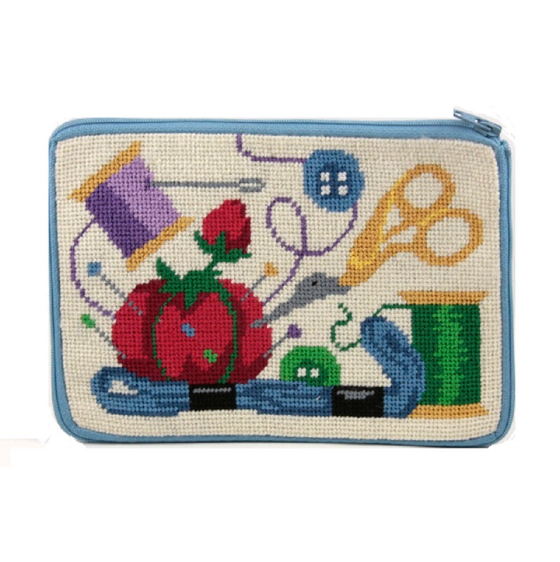 May include: A needlepoint zippered pouch with a white background and a colorful design of sewing supplies, including a spool of thread, a pincushion, scissors, and buttons.