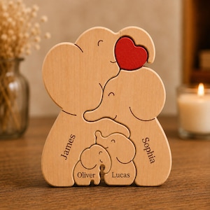 Può includere: Un puzzle in legno di colore chiaro a forma di famiglia di quattro elefanti. I due elefanti più grandi sono incisi con i nomi James e Sophia, mentre i due più piccoli con i nomi Oliver e Lucas. Un cuore rosso è posizionato sulla sommità.