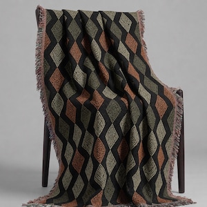 May include: A woven throw blanket featuring a repeating diamond pattern in black, olive green, and burnt orange. The blanket has a textured surface with intricate line details within each diamond shape and finished with fringed edges on the sides.