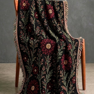 May include: Black throw blanket with a floral pattern in shades of red, gold, and green. The blanket is draped over a wooden chair and has a fringed edge. The floral design features large, detailed flowers and smaller sprigs.