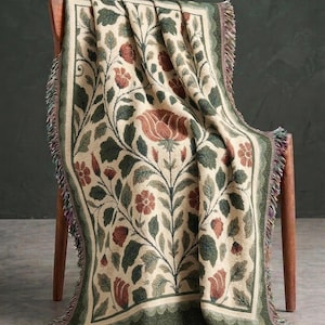 Peut inclure: Un plaid tissé présentant un fond crème avec un motif botanique répétitif de feuilles vert foncé et de fleurs couleur rouille. La couverture possède une bordure décorative et des bords effilochés sur les côtés et l'ourlet inférieur.