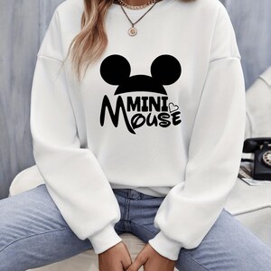 May include: White sweatshirt featuring a black graphic of Mickey Mouse ears and the words "Mini Mouse". The sweatshirt has long sleeves and a crew neck. The design includes a heart symbol.