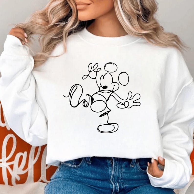 May include: White sweatshirt featuring a black line drawing of Mickey Mouse. The design includes the character's iconic ears, face, and body in a minimalist style. The sweatshirt is a casual, comfortable garment.