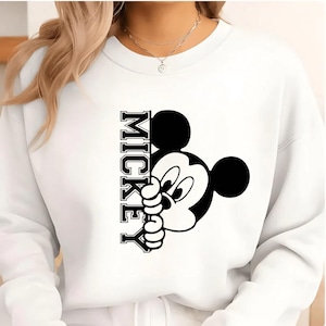 May include: White sweatshirt featuring a black and white graphic of Mickey Mouse peeking out from behind the word "MICKEY" in a vertical, collegiate-style font. The design is centered on the front of the sweatshirt.
