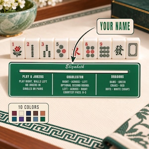 May include: A rectangular green Mahjong card holder with white text featuring sections for Play & Jokers, Charleston, and Dragons. The name Elizabeth is printed in white script. A row of eight white Mahjong tiles with red and green symbols sits above.