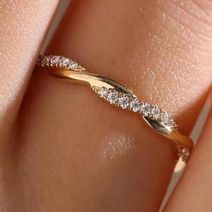May include: A gold ring with a twisted design, featuring small, sparkling stones. The ring's intricate details are highlighted against a blurred background. A delicate piece of jewellery, perfect for everyday wear or special occasions.