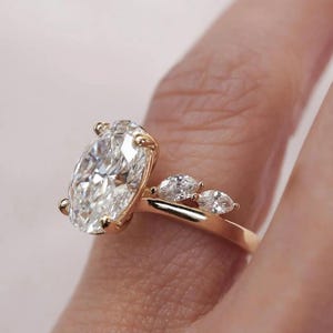 May include: A gold ring featuring a large oval-cut diamond as the centerpiece, flanked by three smaller marquise-cut diamonds. The ring's band is a polished gold, creating a classic and elegant design.