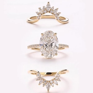 May include: Three gold rings with clear gemstones. The top and bottom rings have a curved design with multiple small gemstones. The middle ring features a large oval gemstone with smaller gemstones along the band.