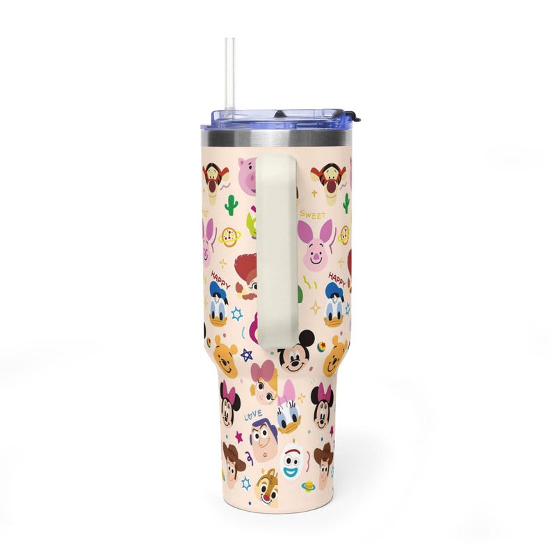 Puede incluir: Un vaso de acero inoxidable de color beige claro con asa y pajita transparente, que presenta un patr&oacute;n repetitivo de caras de personajes de Disney coloridas, incluyendo a Mickey Mouse, el Pato Donald, Daisy, Winnie the Pooh, Tigger y Buzz Lightyear.