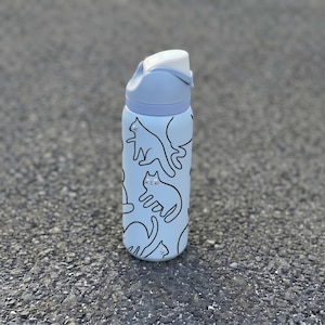 Peut inclure: Une gourde bleu clair avec un couvercle rabattable blanc. La bouteille est ornée d'un motif répété d'illustrations de chats noirs. La bouteille cylindrique semble être en métal.