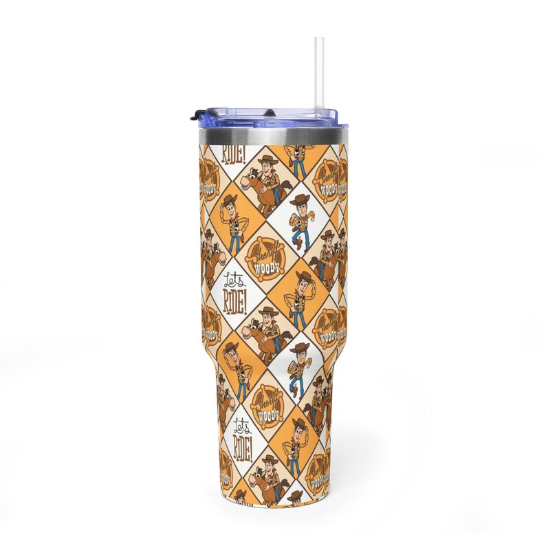 Puede incluir: Un vaso de acero inoxidable con tapa transparente y pajita, con un patr&oacute;n de rombos repetitivo en naranja y blanco. El dise&ntilde;o incluye ilustraciones de un vaquero, estrellas de sheriff y el texto "Let's RIDE!" y "Sheriff Woody".