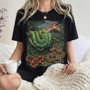 May include: Black t-shirt with a jungle scene featuring three snakes: a green tree snake, a rattlesnake, and a red and black snake. A volcano is visible in the background of the illustration.