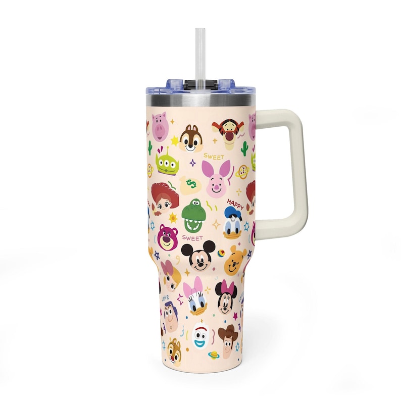Puede incluir: Un vaso de acero inoxidable de color beige claro con asa, tapa transparente y pajita. El exterior presenta un patr&oacute;n repetitivo de caras de personajes de dibujos animados coloridos, incluyendo Mickey Mouse, Minnie Mouse, Donald Duck y varios personajes de Pixar.