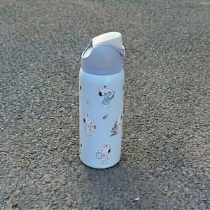 K&ouml;nnte beinhalten: Hellblaue Wasserflasche mit Snoopy-Illustrationen in medizinischer Kleidung. Die Flasche hat einen wei&szlig;en Klappdeckel und ein hellviolettes Band. Die zylindrische Flasche ist wahrscheinlich aus Metall und f&uuml;r Fl&uuml;ssigkeiten bestimmt.