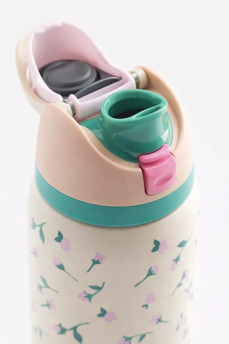May include: A floral-patterned water bottle with a flip-top lid. The lid is a combination of pink, green, and beige. The bottle's body is cream-colored with pink floral accents. The bottle has a pink latch to secure the lid.