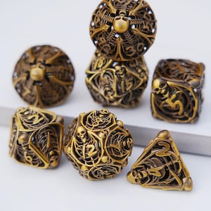 May include: Set of seven antique gold-colored dice with intricate skeletal designs. The dice include various shapes: a d4, d6, d8, d10, d12, d20, and a percentile die. Each die features detailed carvings of skulls and bones, creating a gothic aesthetic.