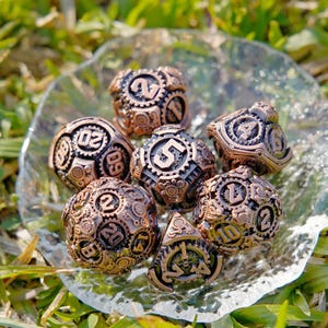 Puede incluir: Un conjunto de dados de estilo steampunk en color bronce, con intrincados detalles de engranajes y números. Los dados están dispuestos sobre un plato redondo y transparente, sobre un fondo de hierba verde. Diseñados para juegos de rol.